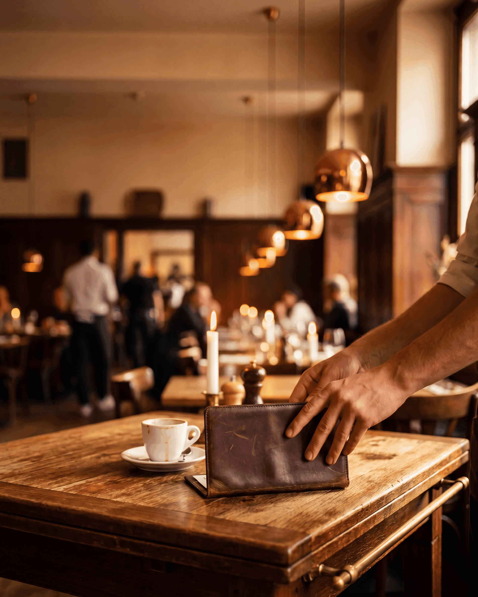Eine Servicekraft legt das Rechnungsmäppchen auf einen Holztisch in einem warmen Schweizer Restaurant zur Abendzeit.